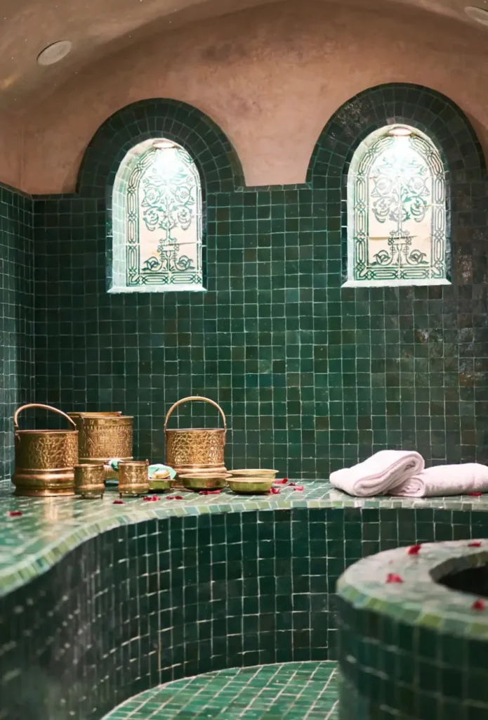Moroccan hammam interior with green zellige tiles, brass water buckets and towels, blending traditional design with contemporary spa comfort