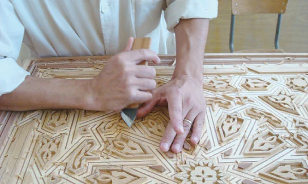 Moroccan artisan hand-carving intricate geometric patterns in wood using traditional craftsmanship techniques