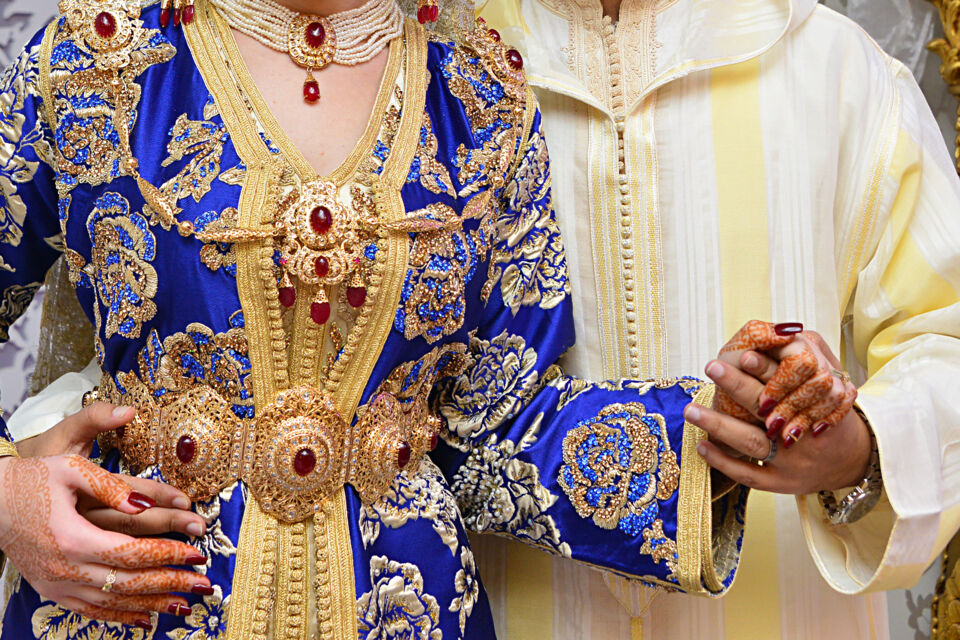 Traditional Moroccan wedding attire featuring an embroidered caftan, golden jewelry, and ceremonial hand henna.